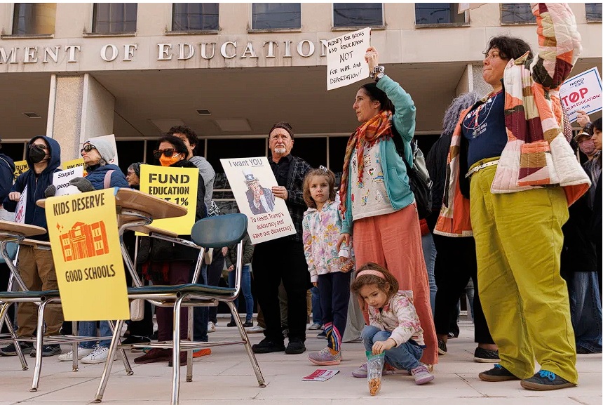 Protesters holding signs in front of the U.S. Department of Education, advocating for educational funding and criticizing budget cuts.